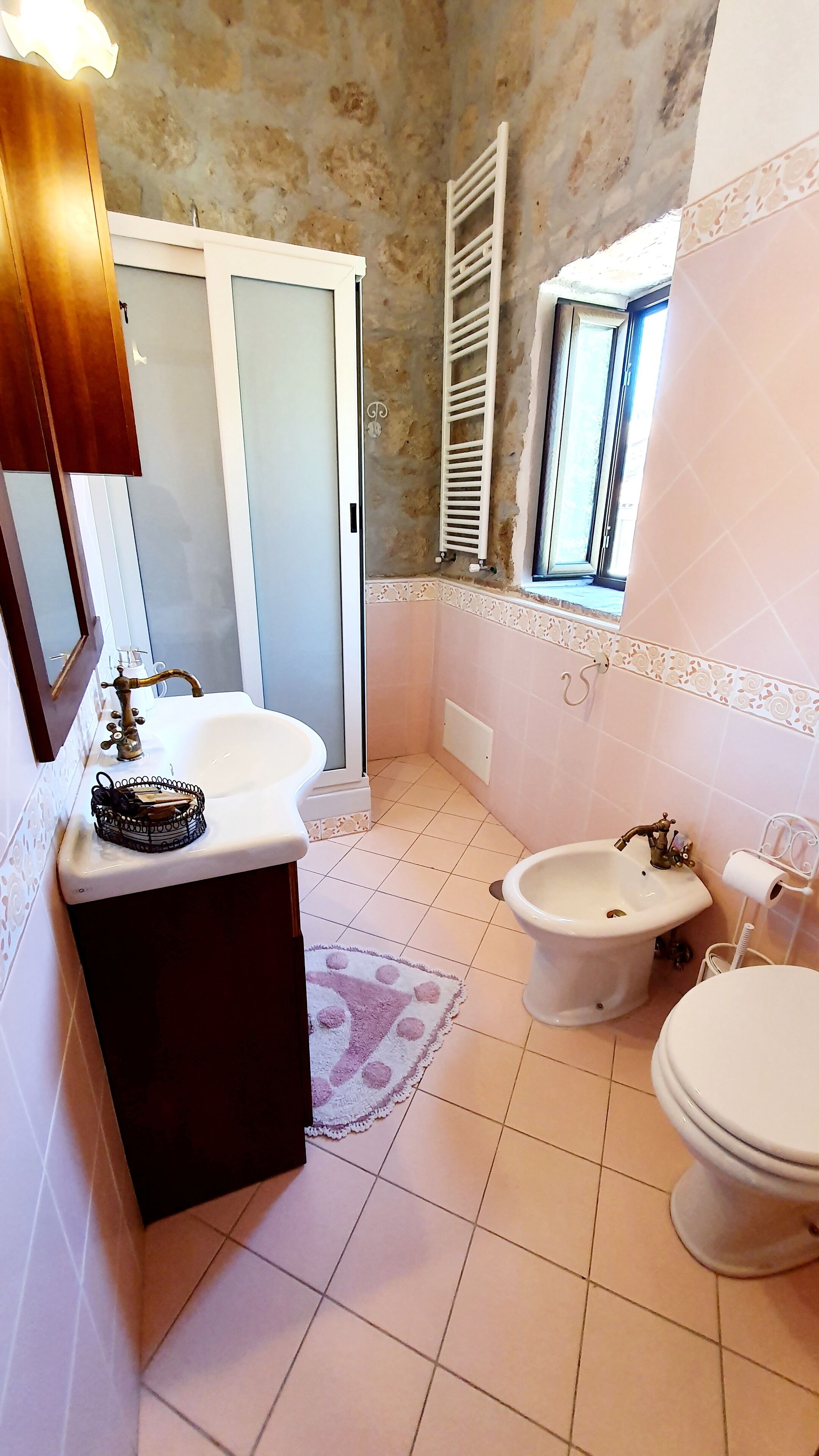 A bathroom with two sinks, a bathtub, and a toilet. There is a shower area with a ladder, and a window providing natural light.