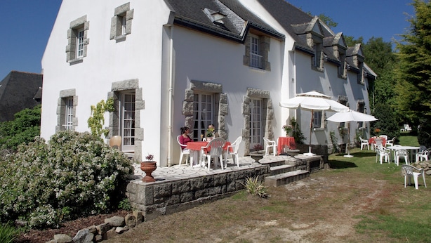 A hotel with a white exterior, stone window frames, and a sign indicating its function. There are outdoor tables and chairs, and a well-maintained garden area. - Hôtel An Ti Gwenn (Carnac)