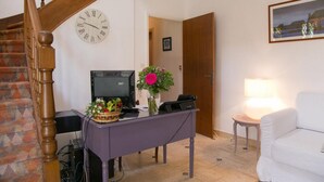 A living room with a wooden staircase, a clock, a desk with a computer, a lamp, and a white couch. - Hôtel An Ti Gwenn (Carnac)