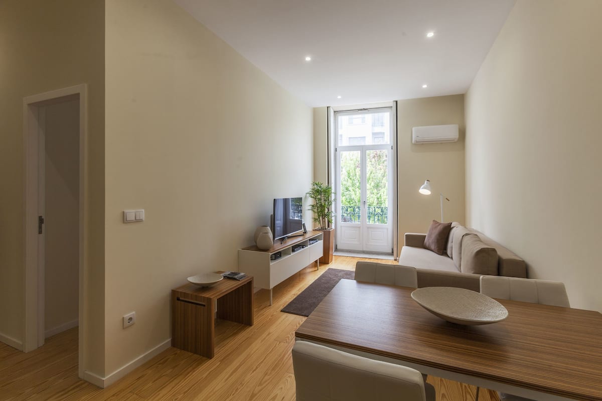 A modern living room with a wooden dining table, a sofa, a TV, and a plant.