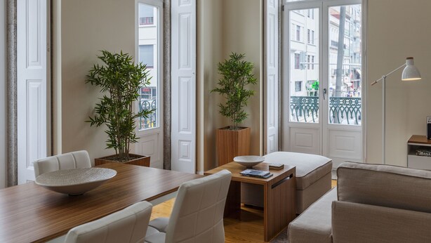 A modern living room with a wooden dining table, white chairs, a sofa, and two potted plants. - BO - Fernandes Tomás (Porto)