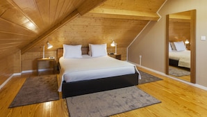 A bedroom with a wooden ceiling, a bed with white bedding, two bedside tables with lamps, and a large mirror on the wall. - BO - Fernandes Tomás (Porto)
