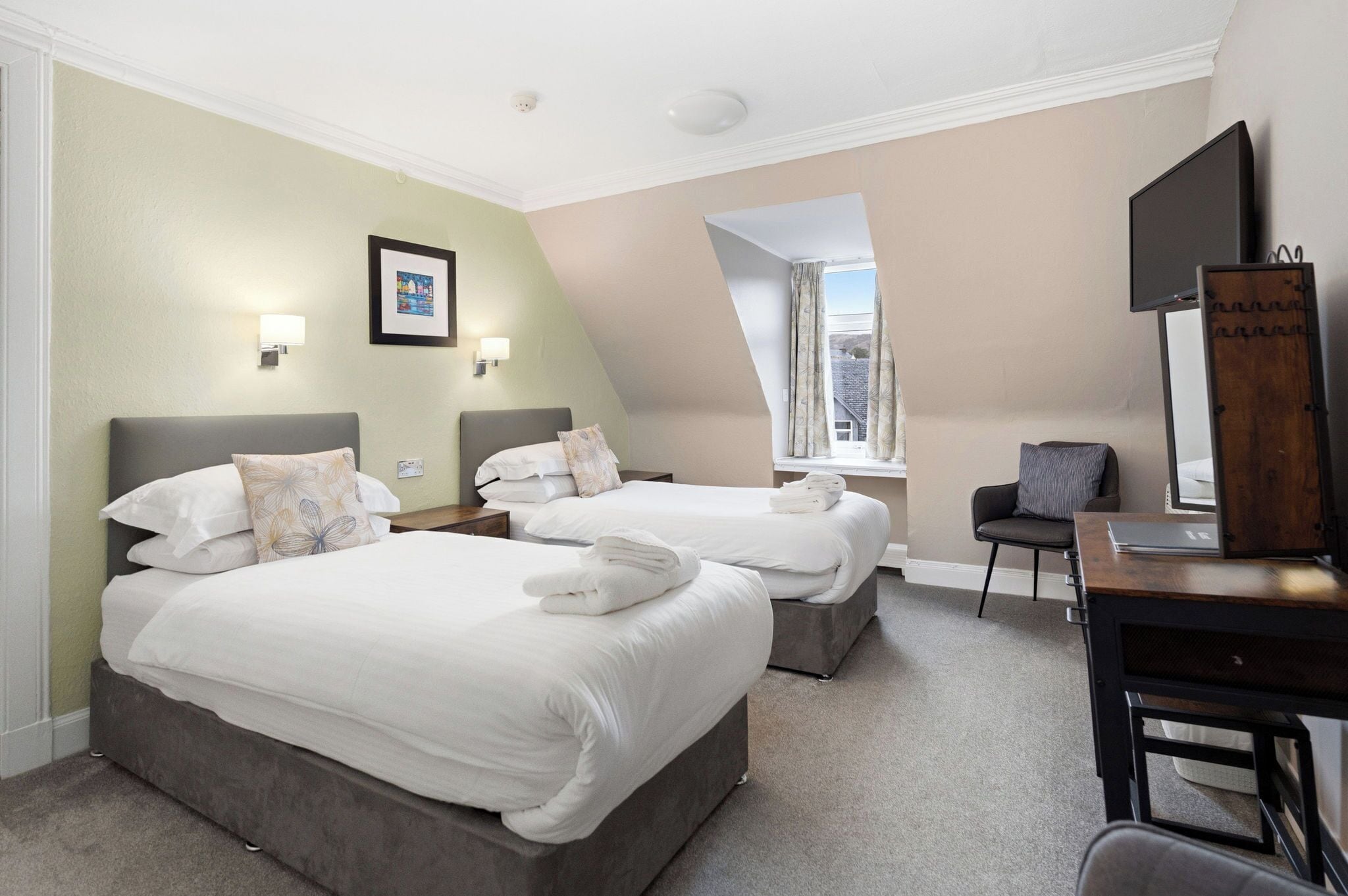A hotel room with two beds, a desk, a chair, a TV, and a window with a view.