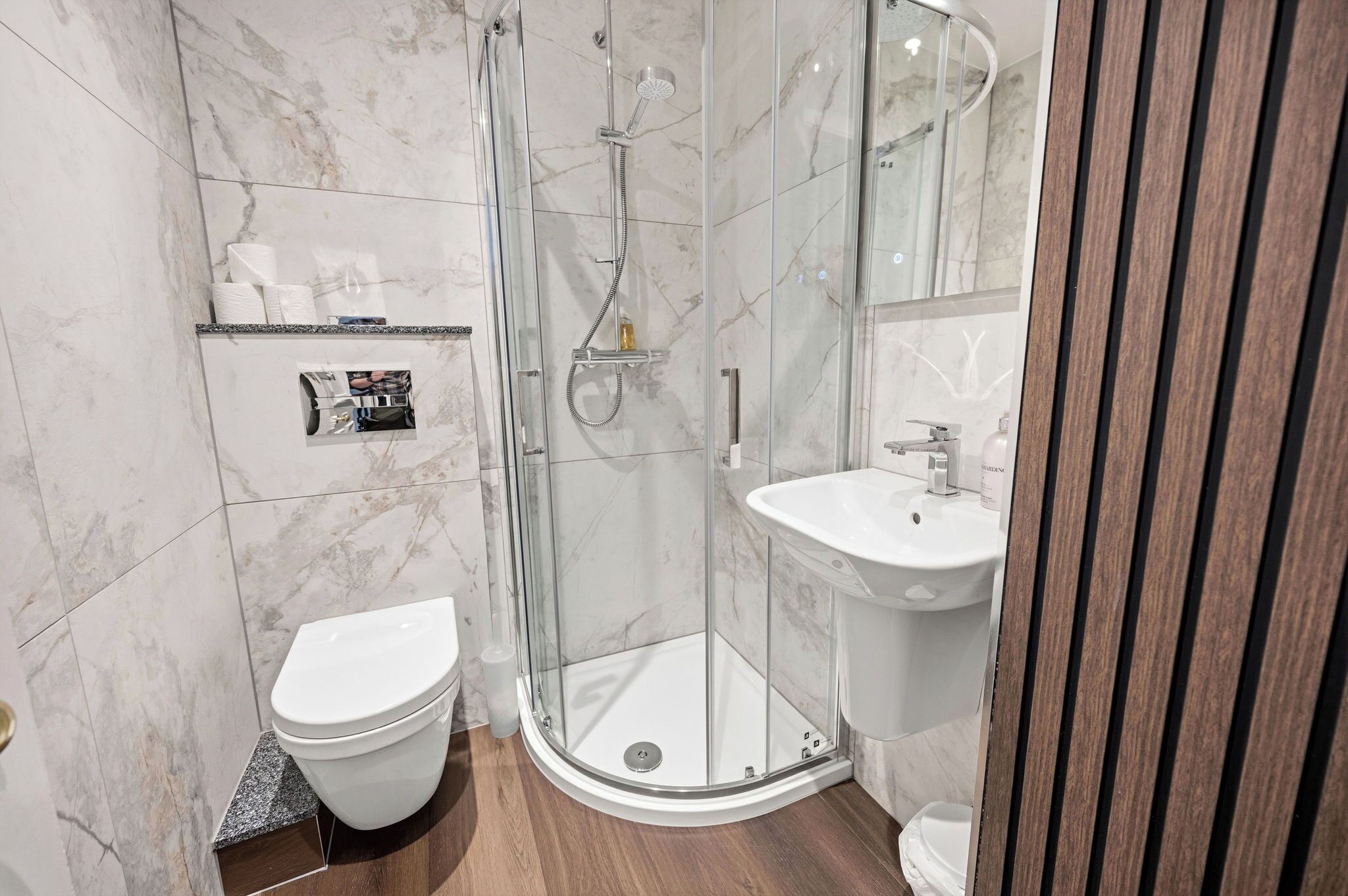 A modern bathroom with a glass-enclosed shower, a white toilet, and a pedestal sink.