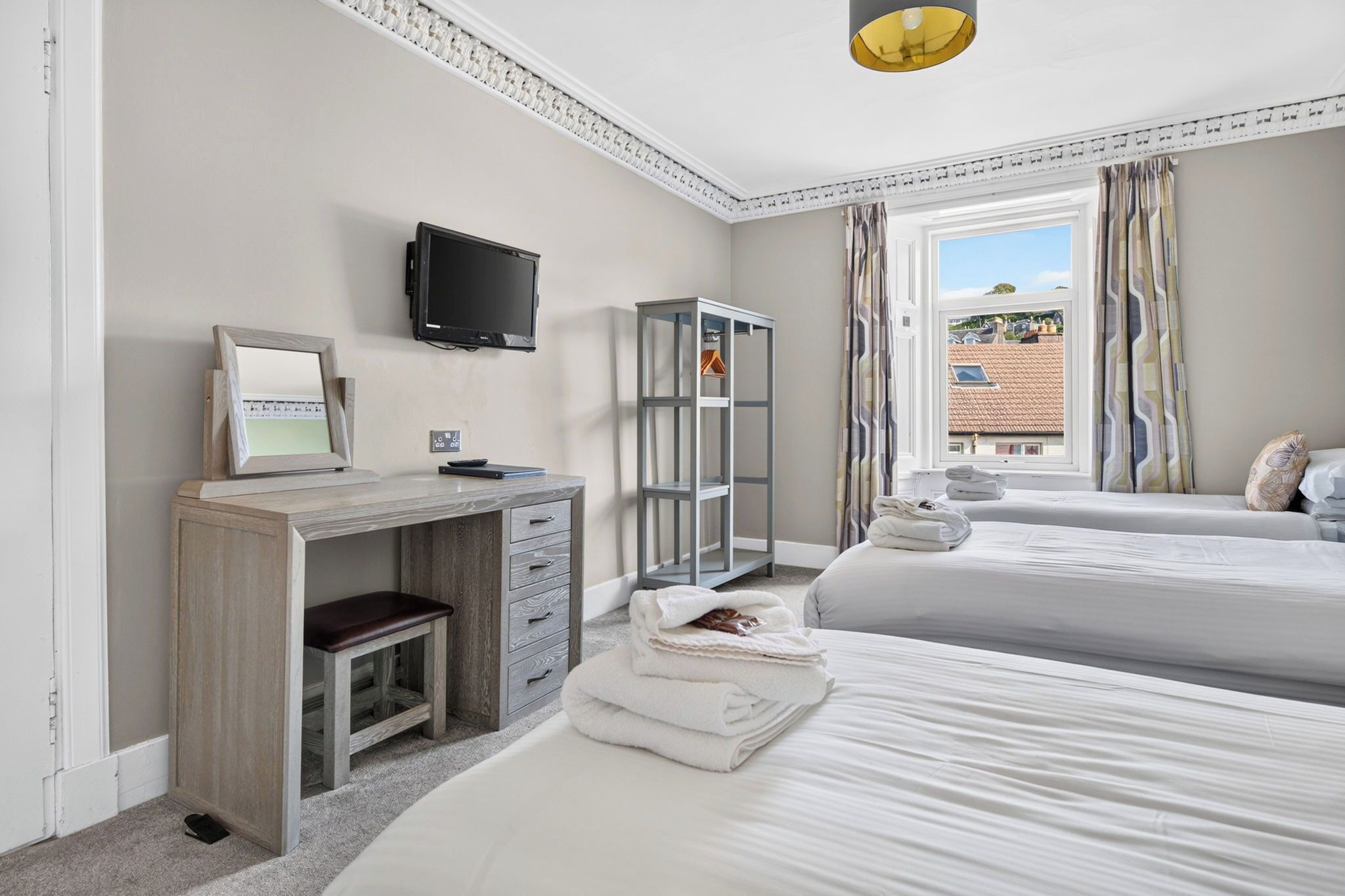 A hotel room with a desk, a television, a wardrobe, two beds, and a window with curtains.