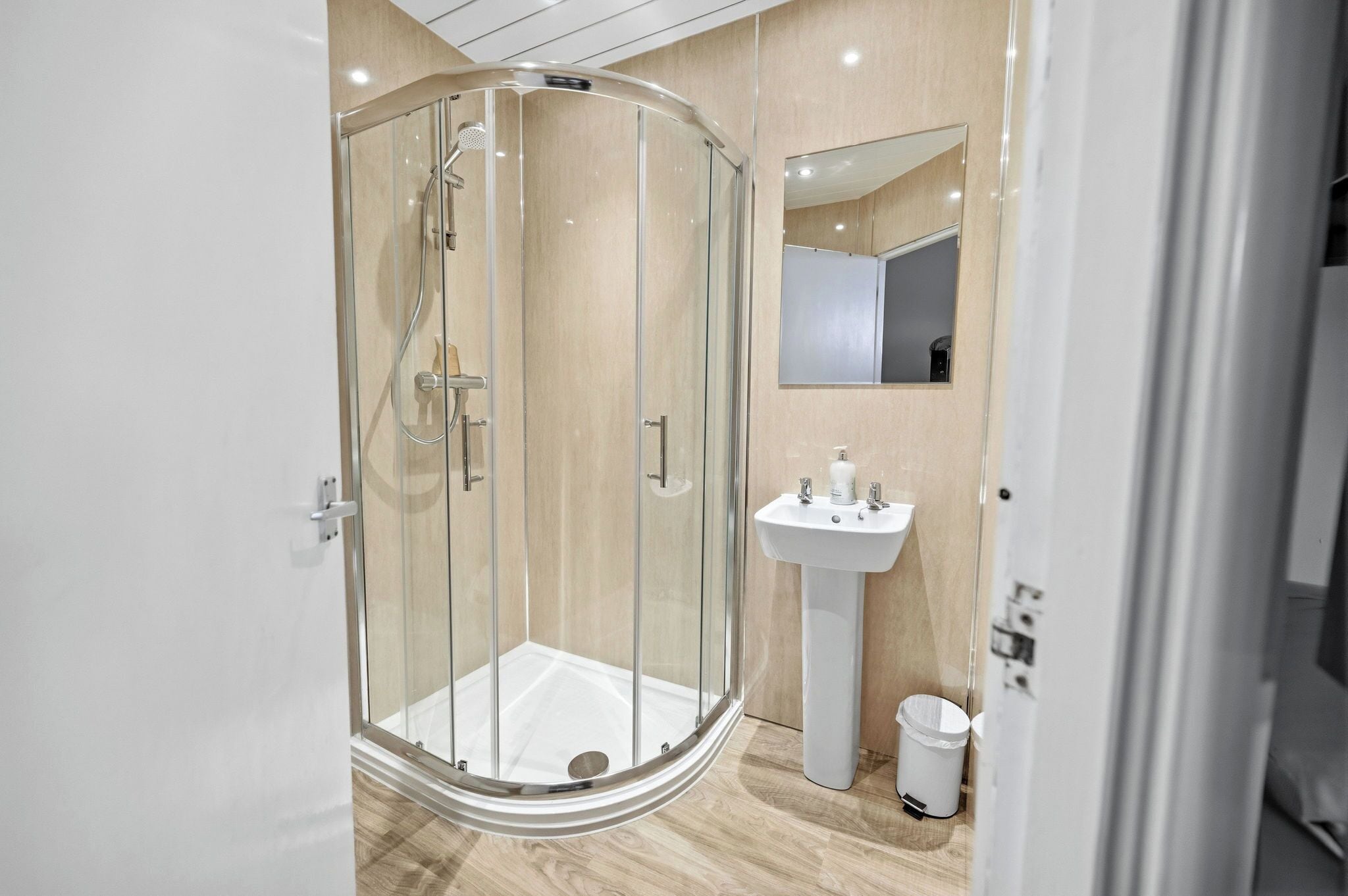 A modern bathroom with a glass-enclosed shower, a pedestal sink, and a mirror above the sink.