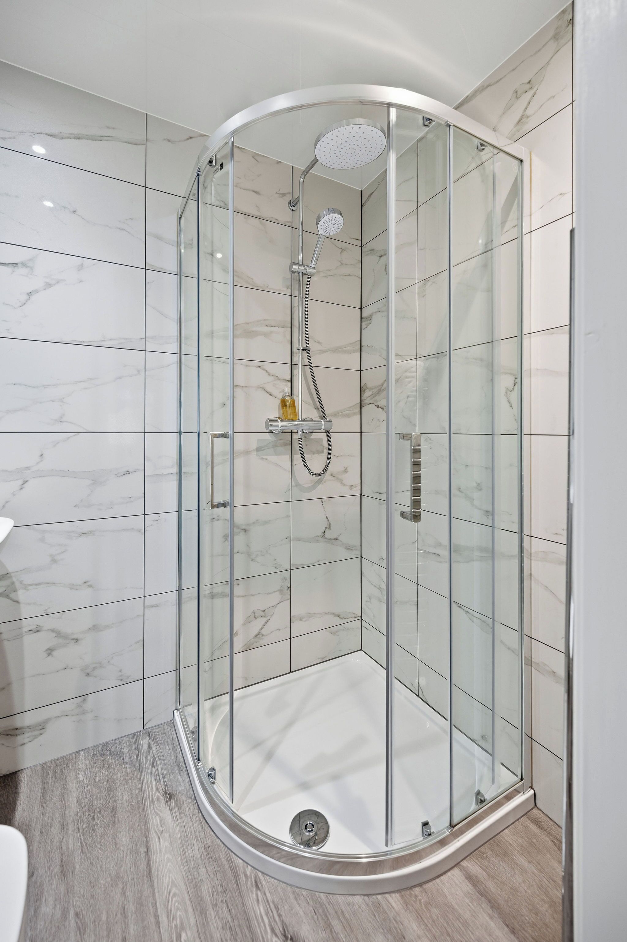 A glass-enclosed shower with a handheld showerhead and a wall-mounted faucet.