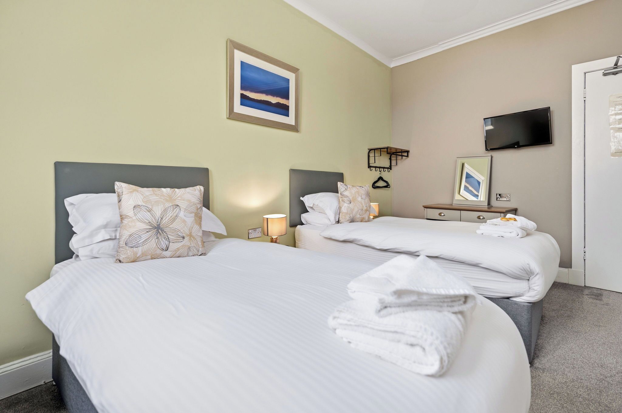 A hotel room with two beds, a television, a framed picture on the wall, and a bedside lamp.