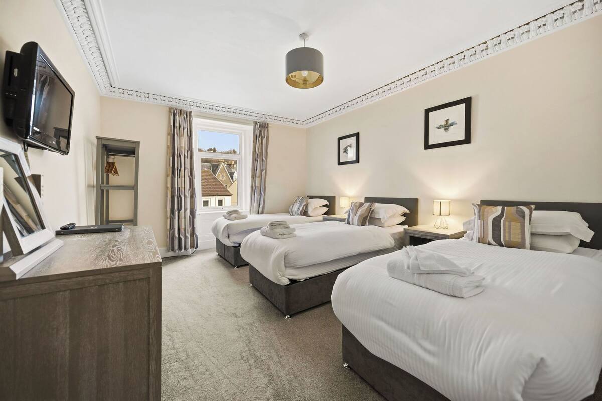 A hotel room with three beds, a TV, a desk, and a window with curtains.
