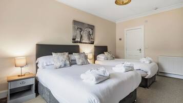A hotel room with two beds, a nightstand with a lamp, a radiator, and a door.