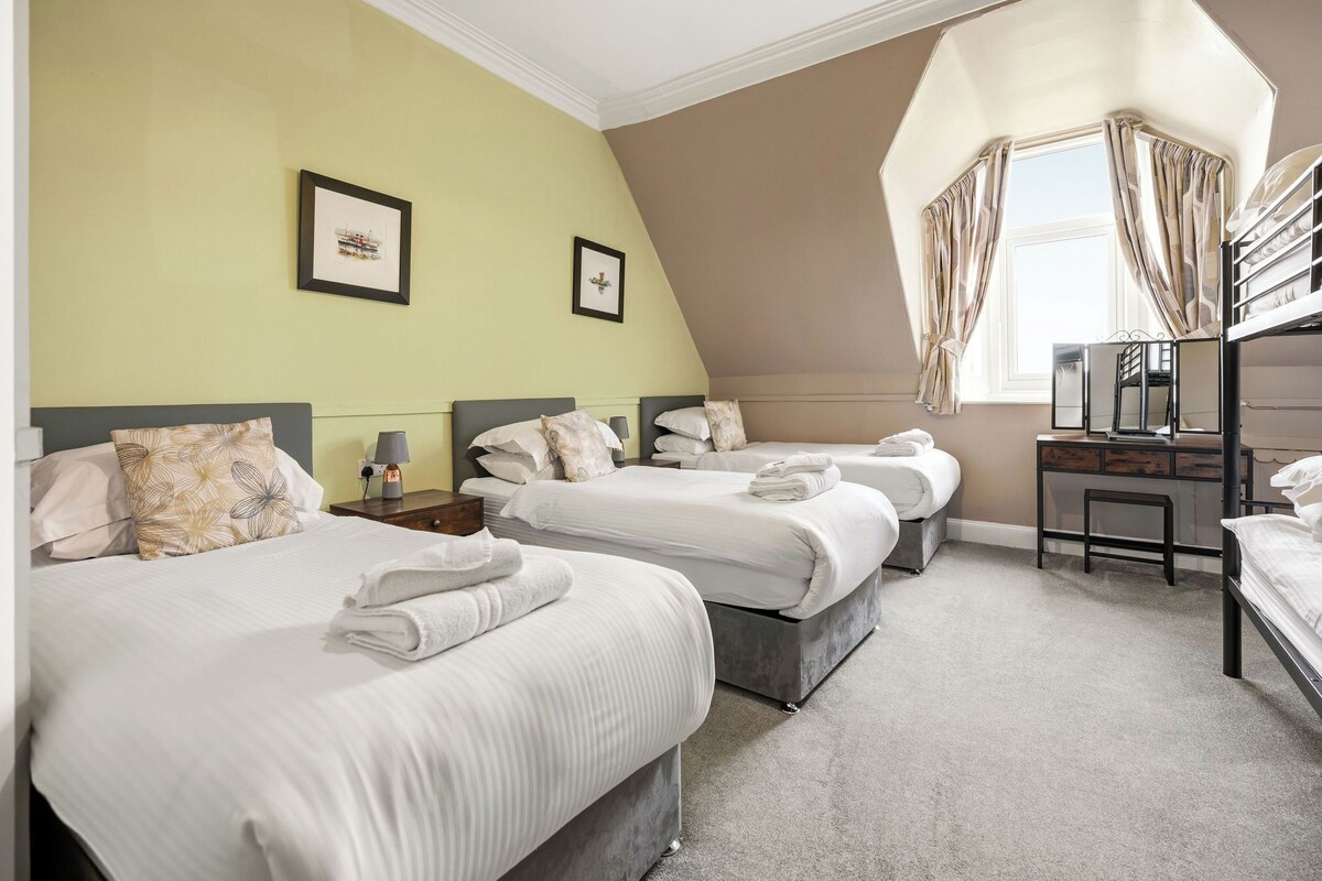 A hotel room with three beds, a desk, and a window with curtains.