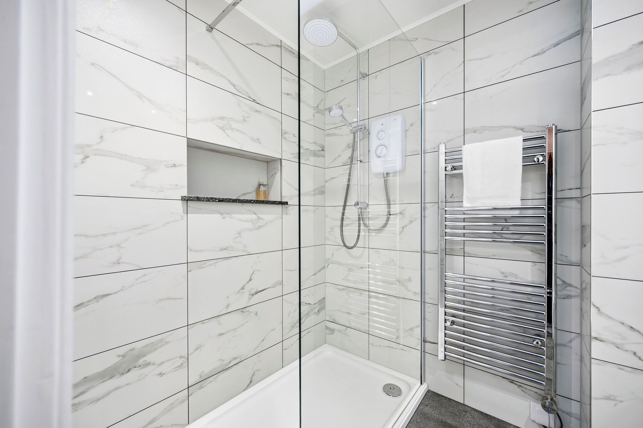 A modern bathroom with a glass-enclosed shower, a built-in towel rack, and a marble-tiled wall.