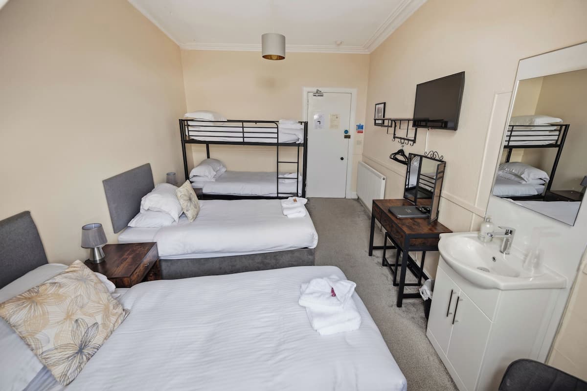A hotel room with two single beds, a desk with a chair, a sink, and a television.