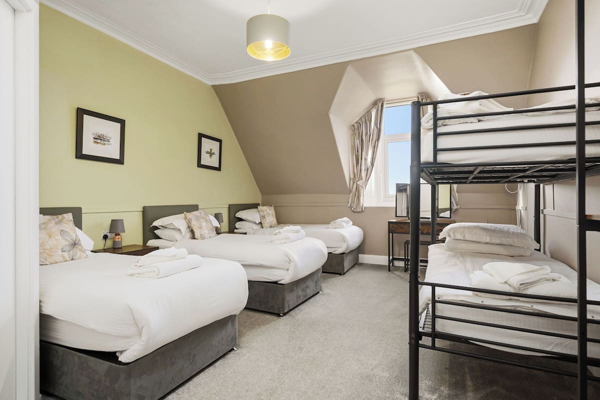A hotel room with two single beds, a bunk bed, a desk, and a window with curtains.