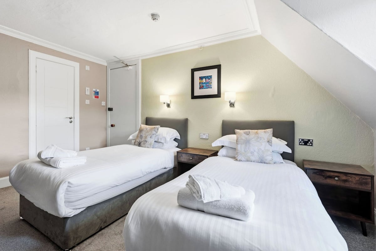 A hotel room with two beds, white bedding, a framed picture on the wall, and a small wooden nightstand.