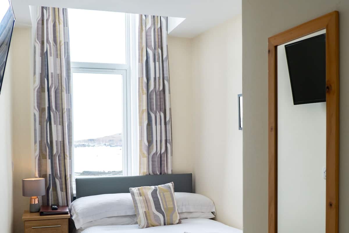 A neatly arranged bedroom with a bed, bedside table, lamp, and a large mirror.