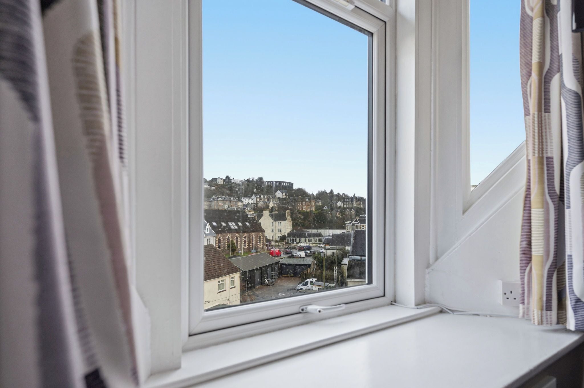 A window with a view of a residential area, a white window frame, and a curtain partially visible.