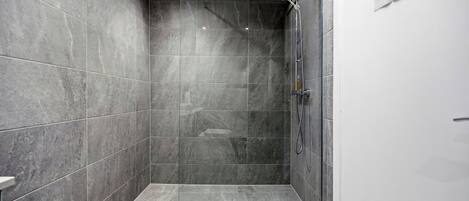 A modern shower area with grey tiles, a glass door, and a sign indicating 'Rooms 3-5, 6-8, 9-11, 12-14, 15-17, 18-20, 21-23, 24-26, 27-29, 30-32, 33-35, 36-38, 39-41, 42-44, 45-47, 48-50, 51-53, 54-56, 57-59, 60-62, 63-65, 66-68, 69-71, 72-74, 75-77, 78-80, 81-83, 84-86, 87-89, 90-92, 93-95, 96-98, 99-101, 102-104, 105-107, 108-110