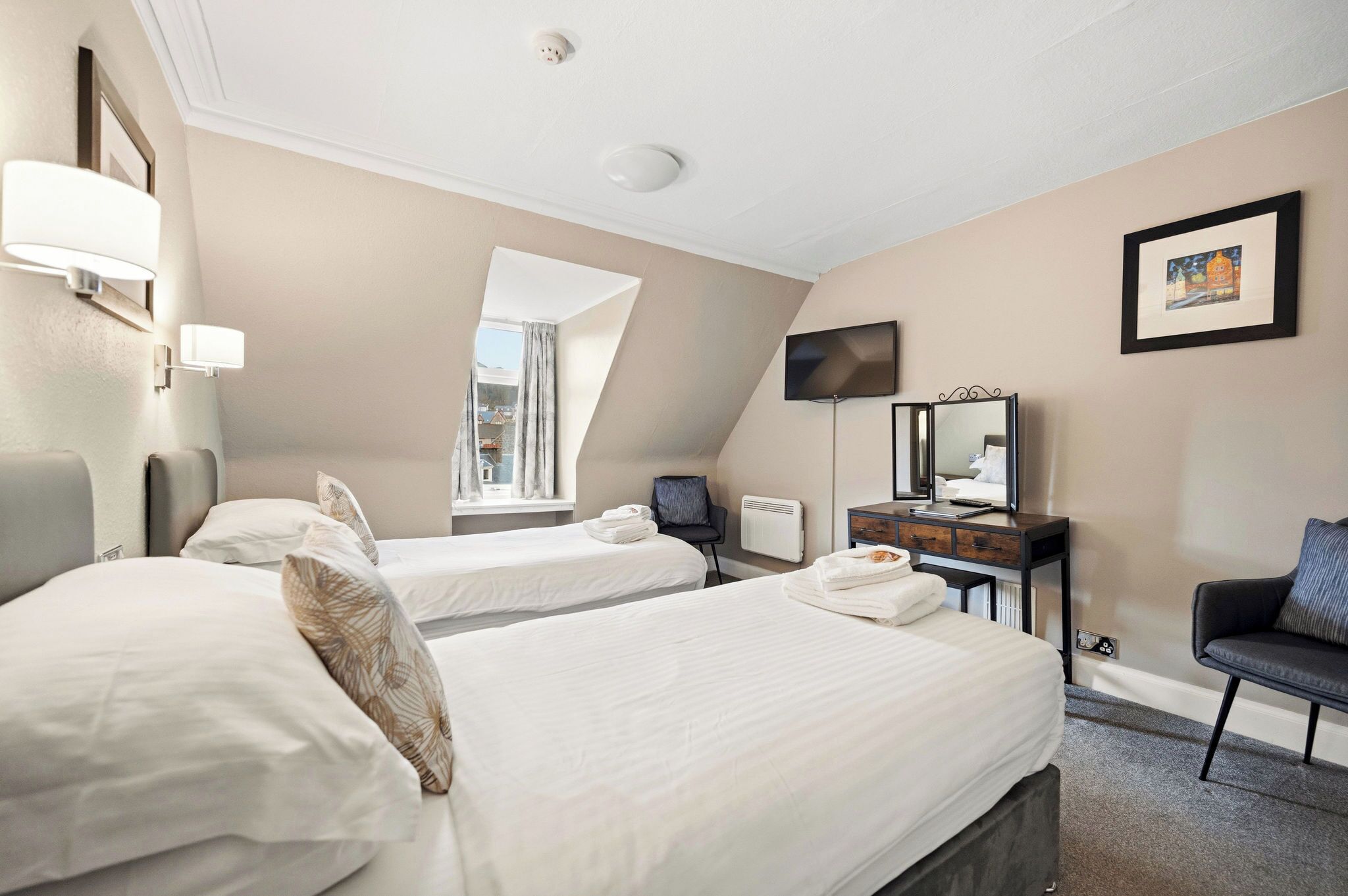 A hotel room with two beds, a desk, a chair, a TV, and a window.
