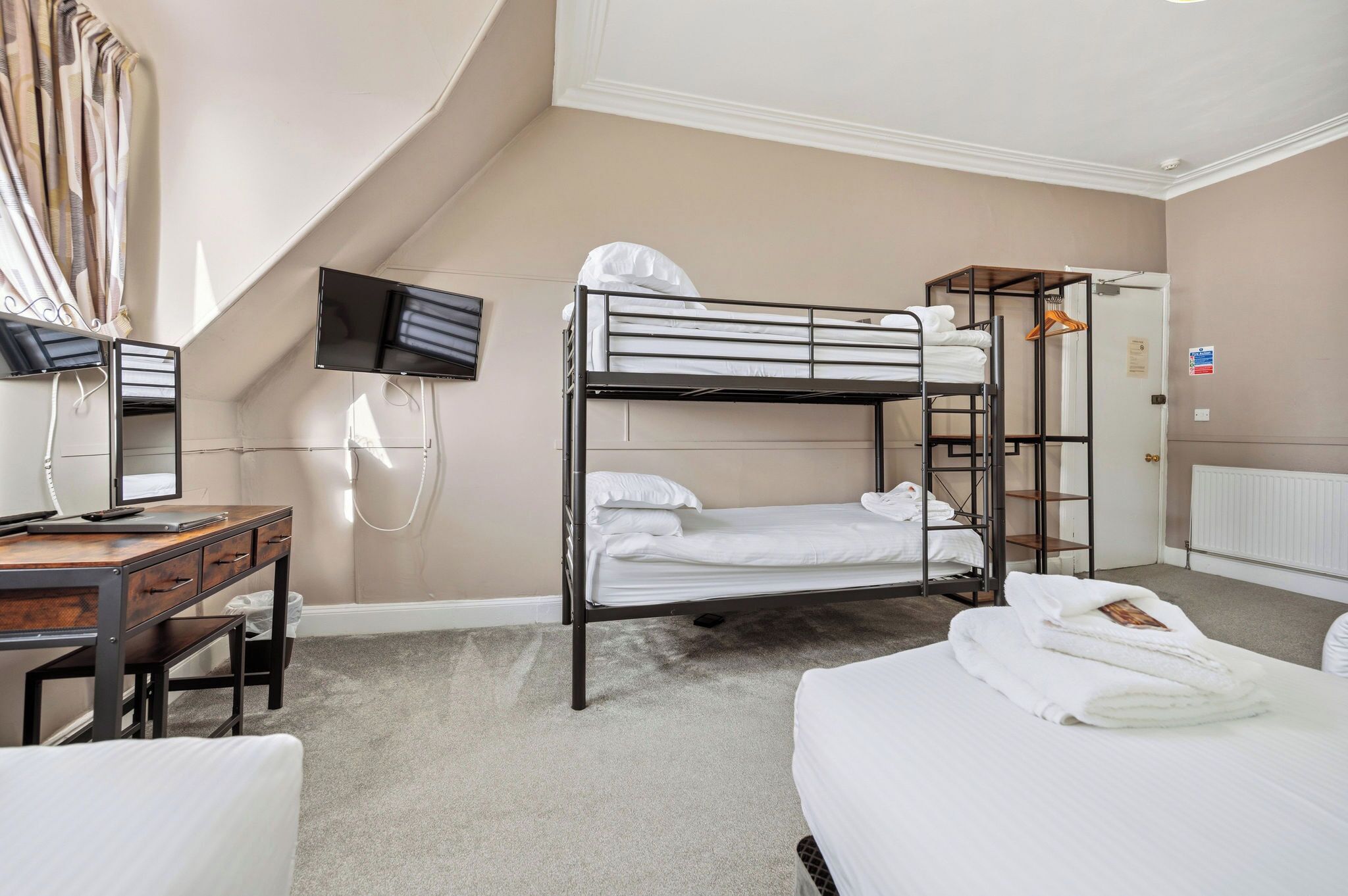 A hotel room with bunk beds, a desk with a computer, a TV, and a wardrobe.