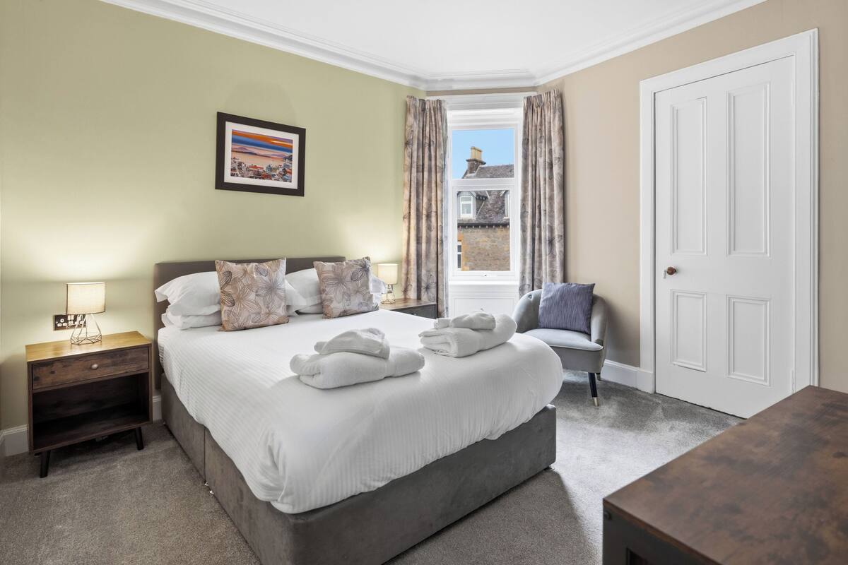 A bedroom with a bed, nightstand, chair, and a door.