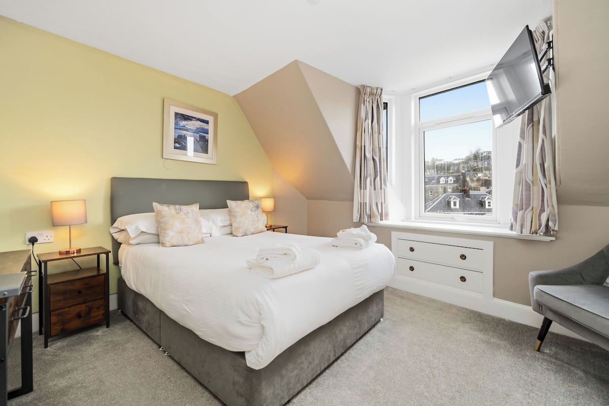 A neatly arranged bedroom with a bed, bedside tables, a TV, and a window with curtains.