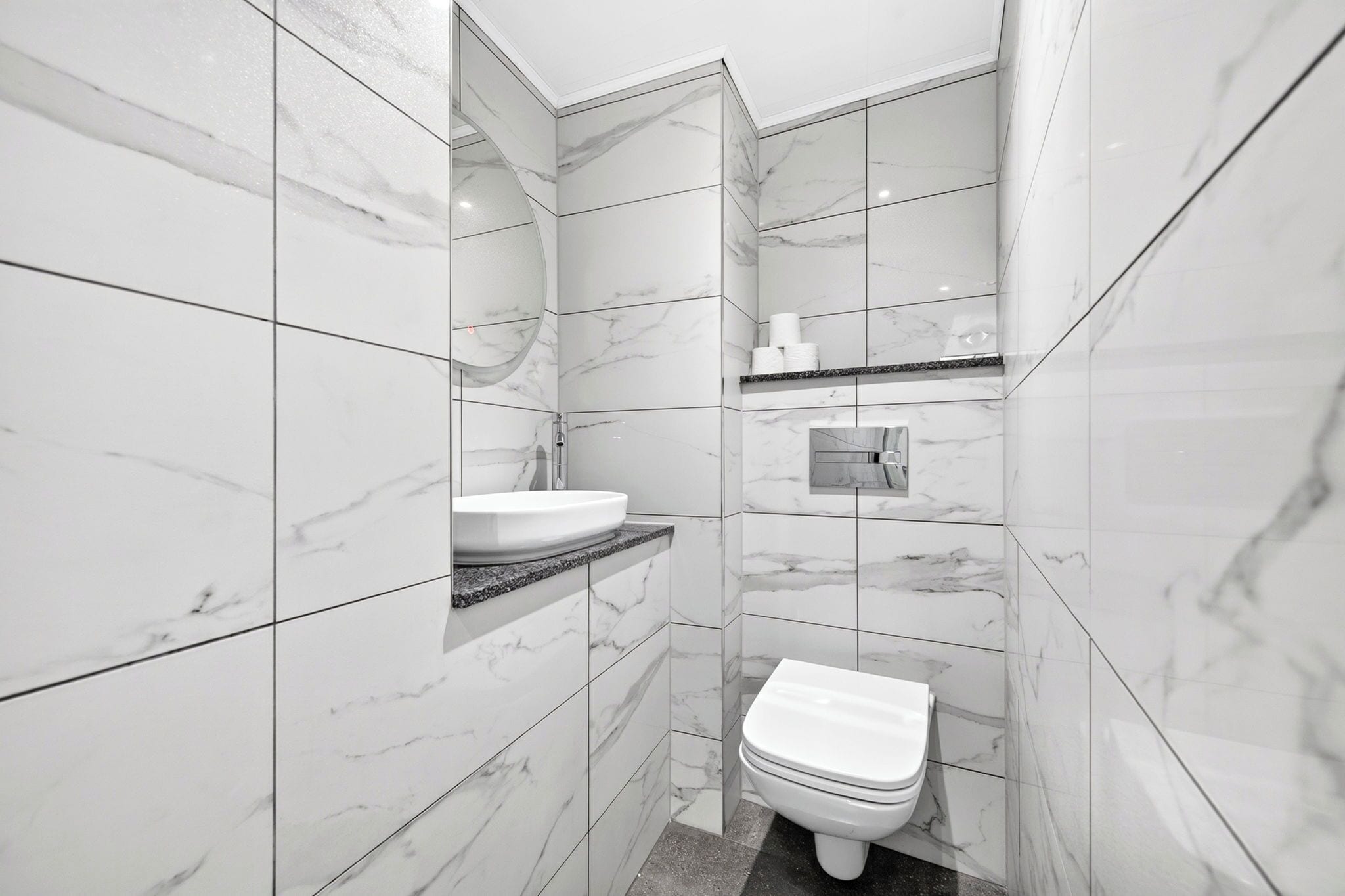 A modern bathroom with a marble wall, a sink, and a toilet.