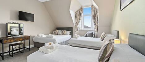 Une chambre d’hôtel avec deux lits, un bureau avec un ordinateur, un téléviseur fixé au mur et une fenêtre avec des rideaux.