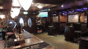 A bar area with a wooden counter, bar stools, and a large screen displaying a sports game. - Corran House Guest House (Oban)