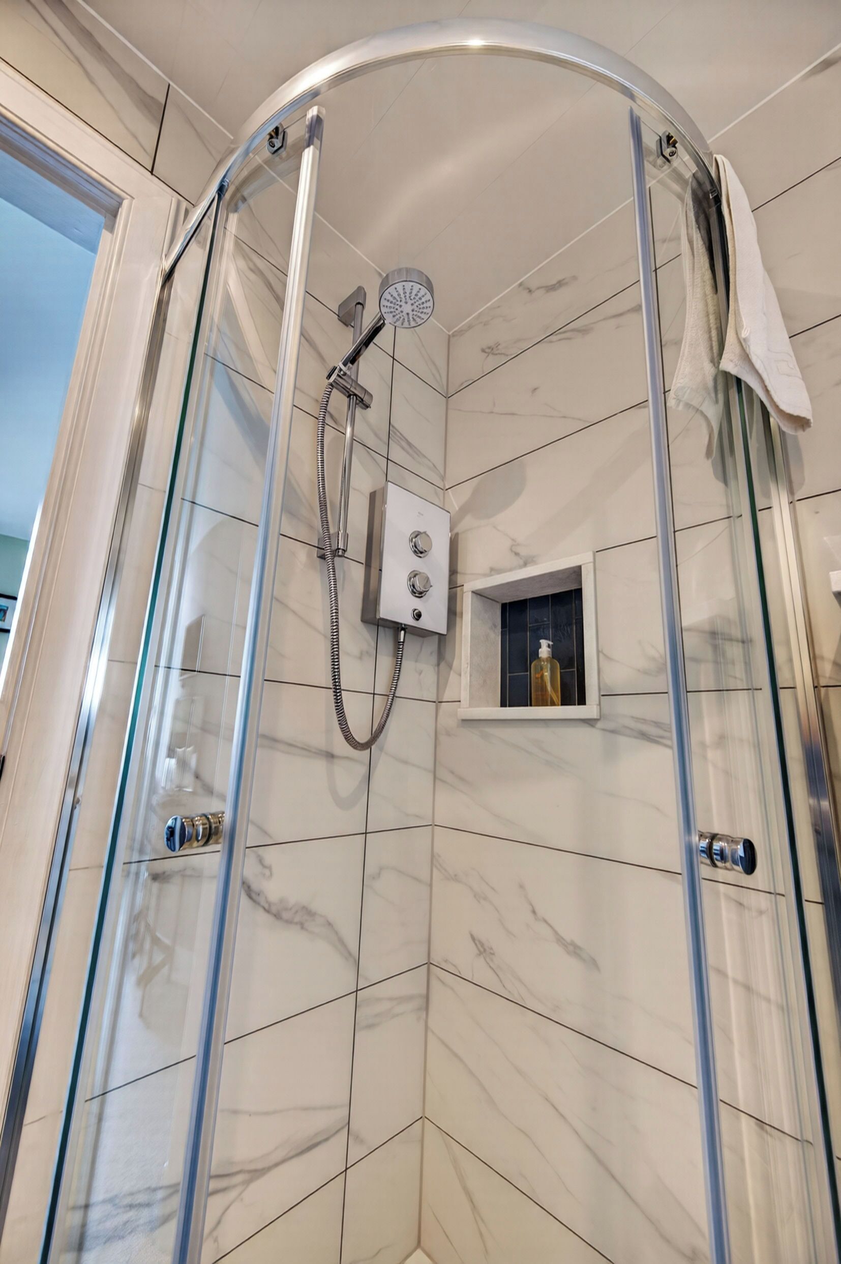 Eine Eckdusche mit Glastür, Duschbrausehandstück und Bedienfeld.