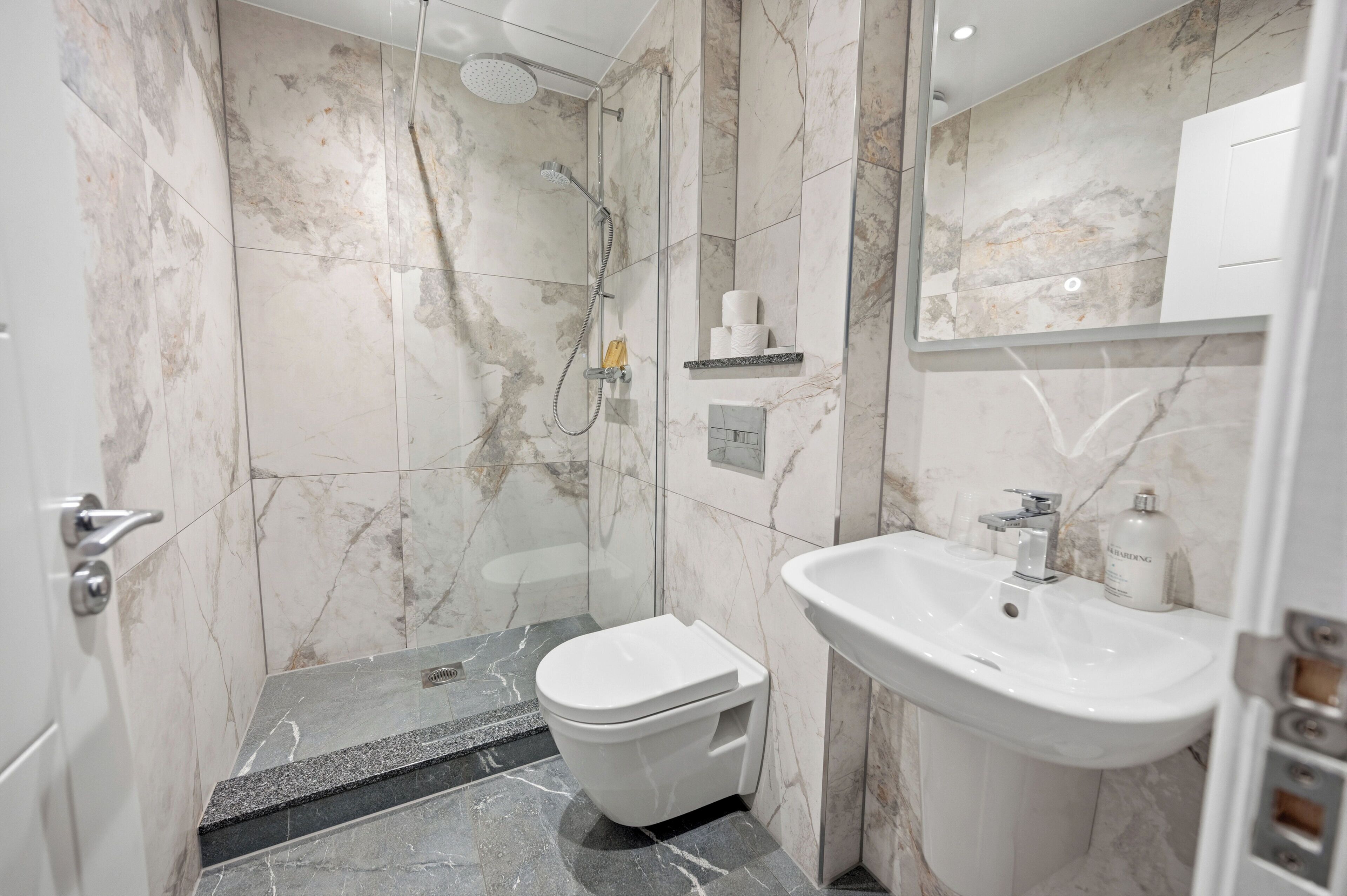 A bathroom with a shower, toilet, sink, and marble walls.