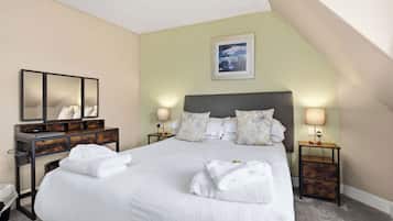 A neatly made bed with white linens, a wooden dresser with a mirror, two bedside tables with lamps, and a framed picture on the wall.