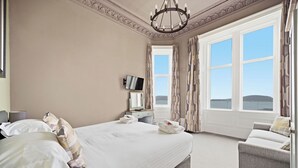 A bedroom with a large bed, a TV, a desk, and a view of the sea. - Corran House Guest House (Oban)