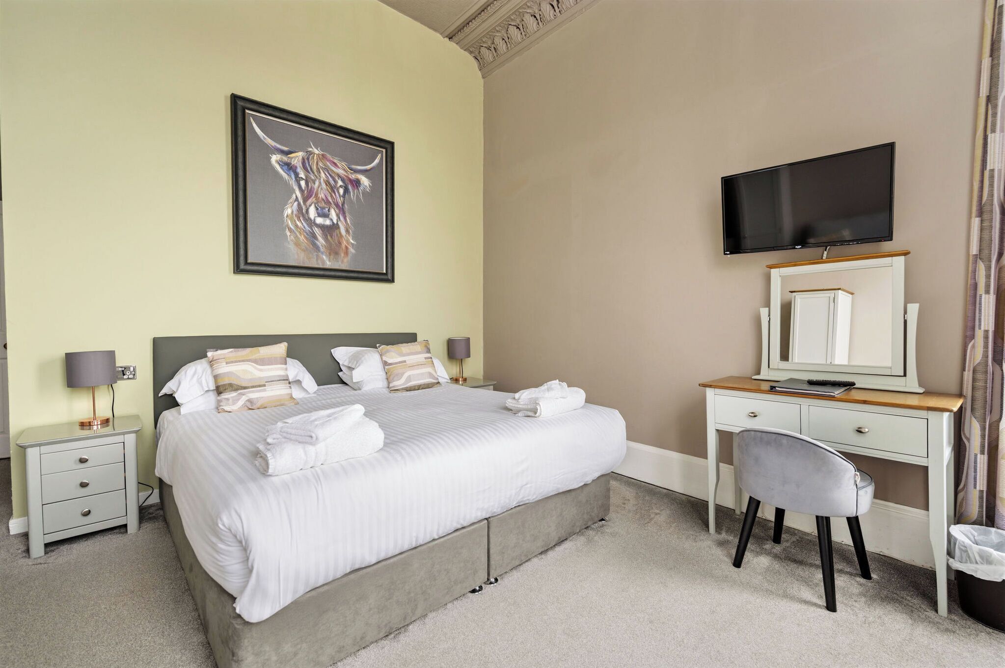 A hotel room with a bed, a desk, a television, a painting, and a chair.