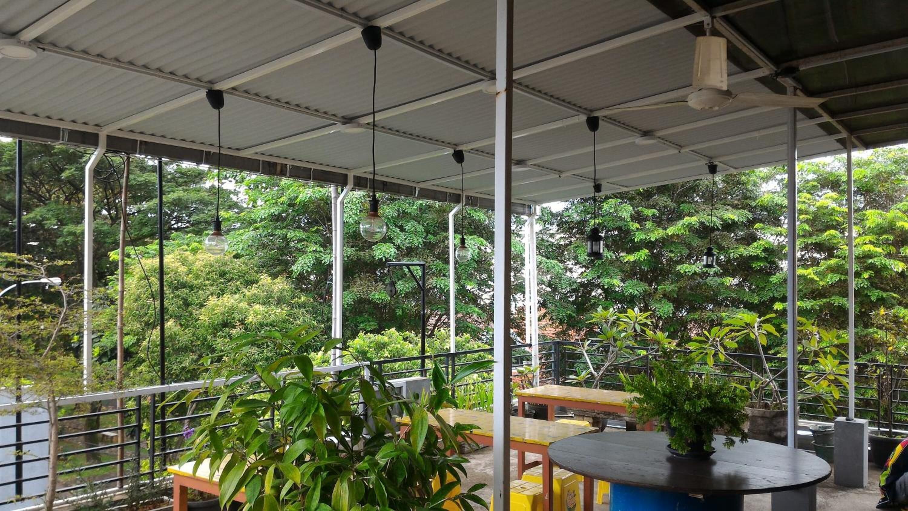 An outdoor patio with tables and chairs, surrounded by lush greenery and trees.