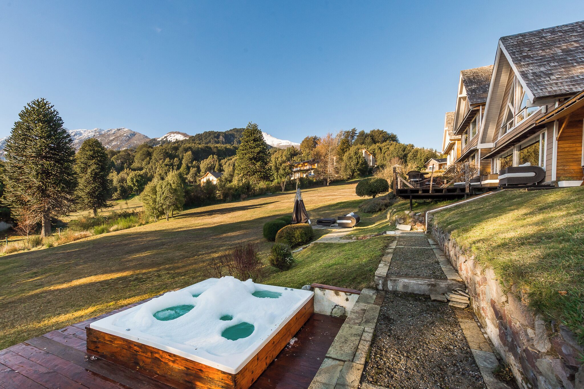 Un jacuzzi en una terraza de madera con vistas a un paisaje montañoso y una hilera de casas.