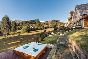 Uma banheira de hidromassagem em um deck de madeira, com vista para uma paisagem montanhosa e uma fileira de casas.
