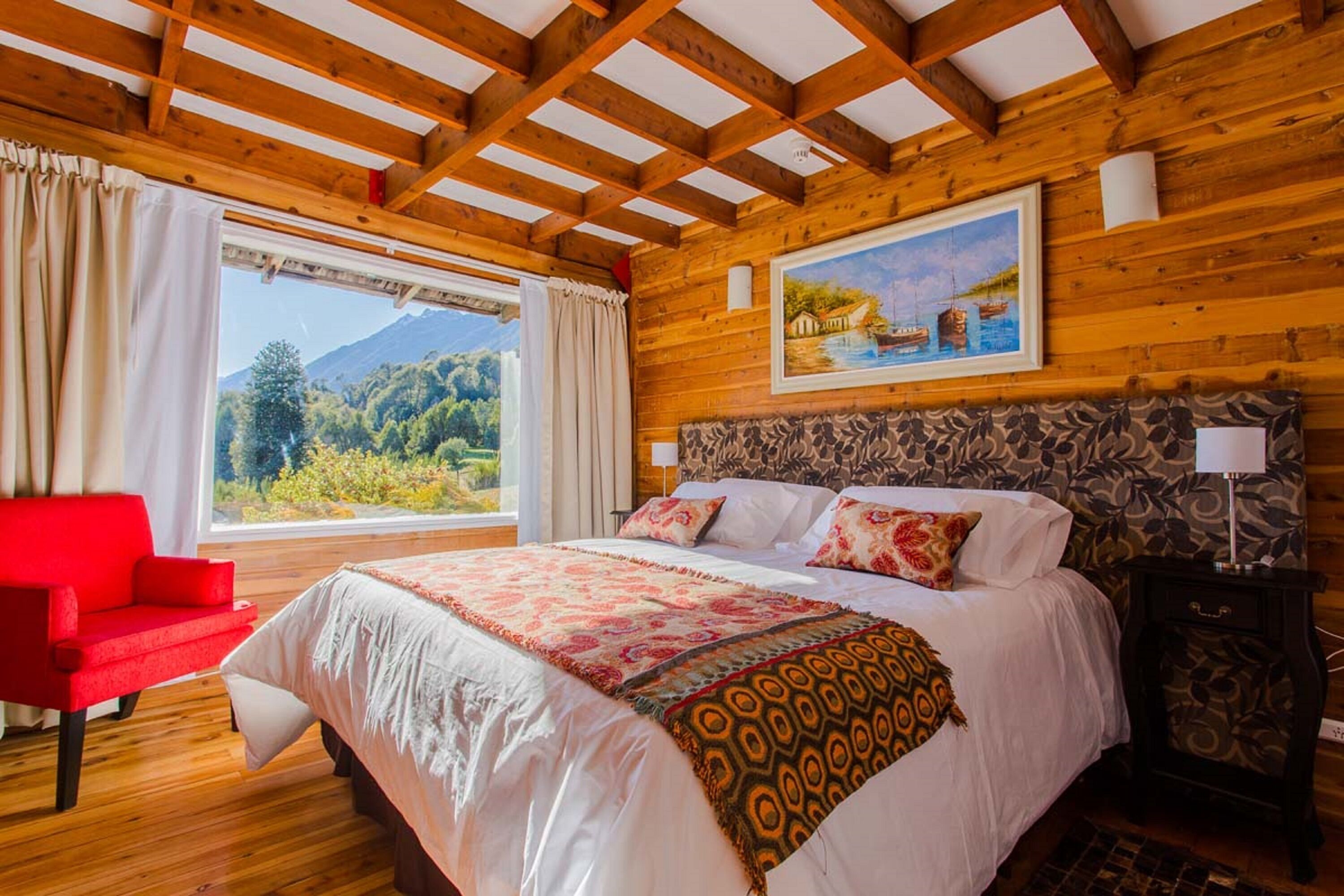 Un dormitorio con paneles de madera, una cama grande, una silla roja, una mesita de noche y un cuadro de un paisaje.