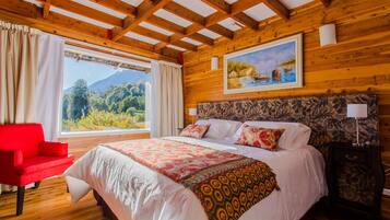Un dormitorio con paneles de madera, una cama grande, una silla roja, una mesita de noche y un cuadro de un paisaje.