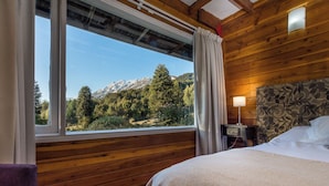 Une chambre rustique en bois, avec un lit, une table de chevet et une fenêtre donnant sur une forêt et des montagnes.