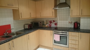 Eine Küche mit Holzschränken, einer Mikrowelle, einem Toaster, einem Wasserkocher und einem Spülbecken.