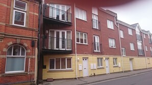 En flervåningsbostadsbyggnad med röda tegelväggar, vitmålade fönsterkarmar och balkonger med svarta räcken.