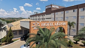 Entrada de un hotel con un letrero que dice 'HOTEL LIGUORI', rodeada de palmeras y coches aparcados.