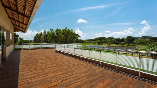 A wooden deck with a metal railing overlooking a river and greenery. - Liguori Hotel (Trindade)