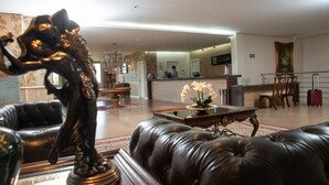 A lobby with leather sofas, a reception desk, a chandelier, and a painting on the wall. - Liguori Hotel (Trindade)