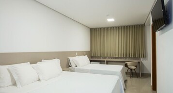 Habitación de hotel con dos camas, un escritorio, una silla y una ventana con cortinas.