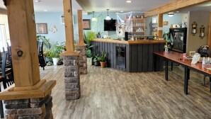 A restaurant with a wooden bar, stone pillars, and a counter with a menu board. - North Shore Wayside Inn (Blind River)