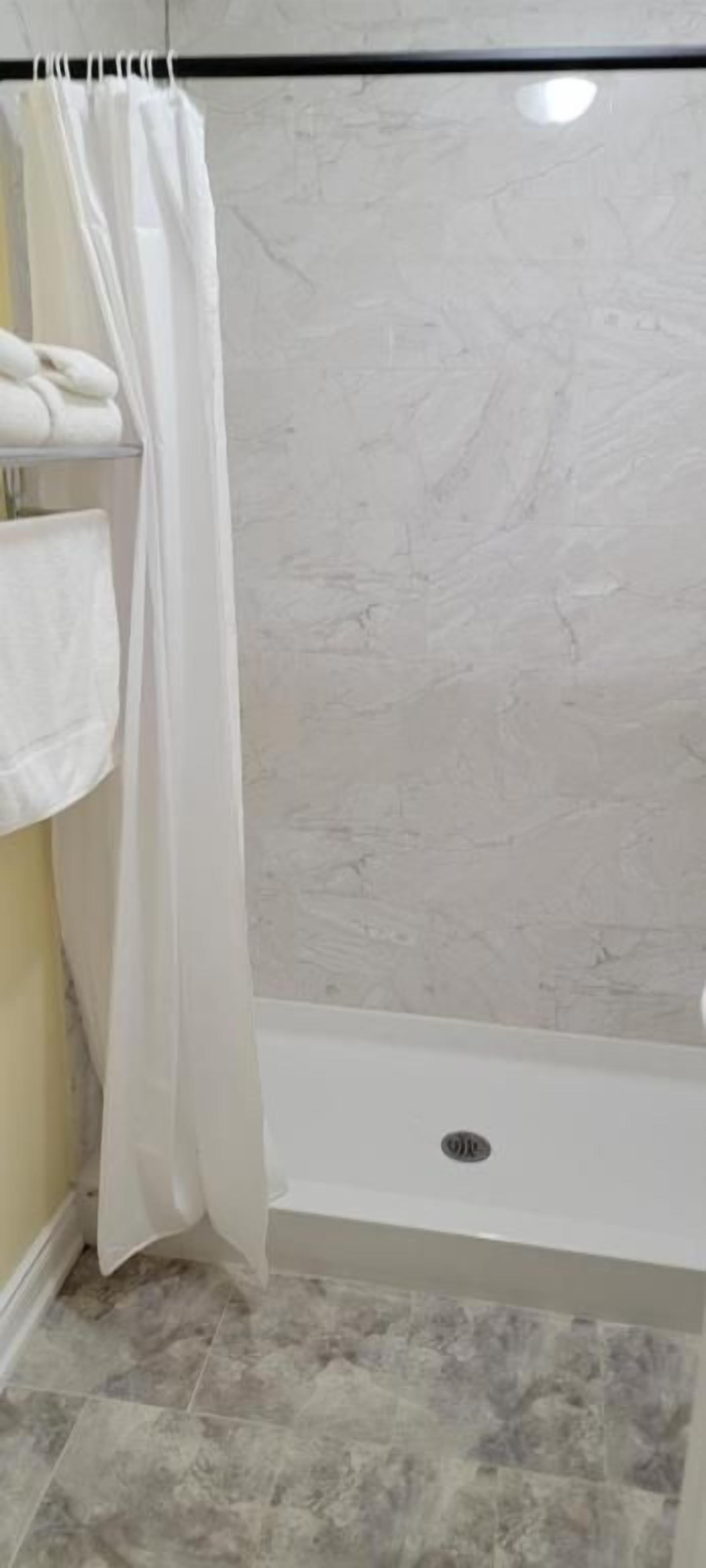 A bathroom with a shower area, a towel rack, and a tiled floor.