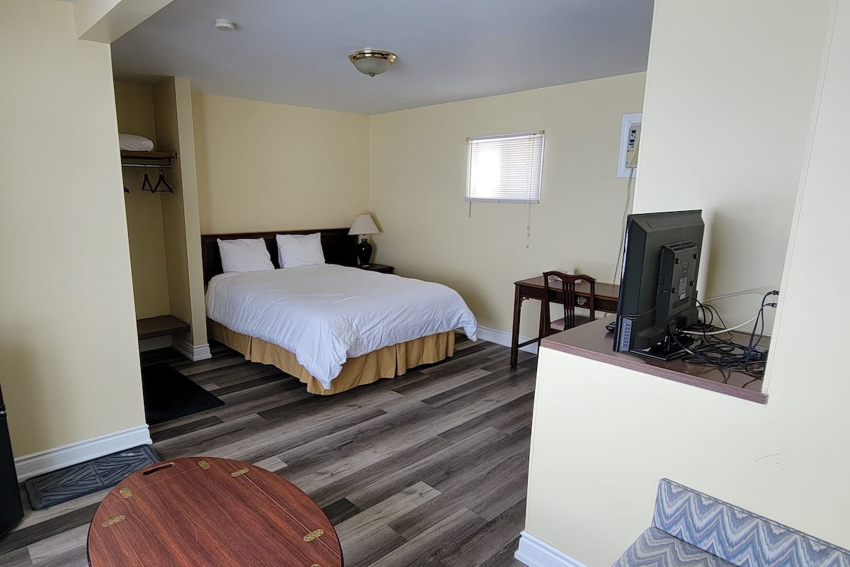 A hotel room with a bed, a desk with a computer, a small table, and a wardrobe.