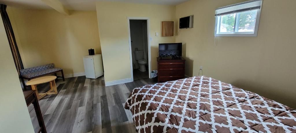 A bedroom with a bed, a bench, a small cabinet, a television, and a window.